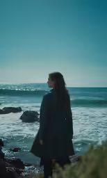 a woman standing near the ocean looking at the waves