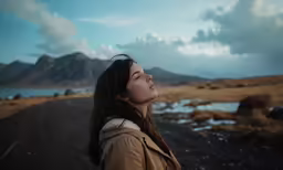 a young lady looks at the sky, overlooking a lake and mountains