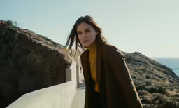 the girl is standing on a white wall by the ocean