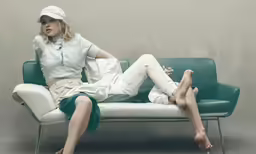 a woman sitting on a couch in white shirt and white skirt