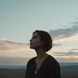 a woman looking up at the sky while standing in the prairie