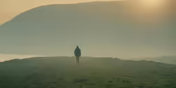the person walks on a grassy hill at sunset