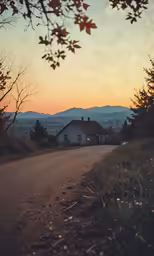 a small house in the middle of a dirt road with mountains in the distance