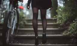 girl in stockings and knee socks walking on stairs next to a bicycle