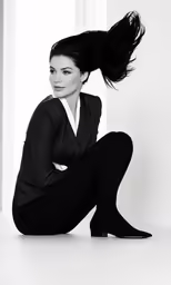 a woman in black sits on the floor with her hair flying in the air