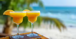 two drinks sitting on top of a table near the ocean