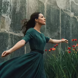 a beautiful young woman in a dark green dress walking by red flowers