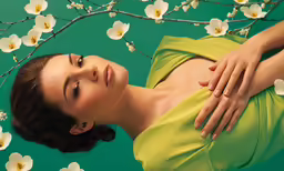 a woman with dark hair wearing a yellow dress is next to a tree with white flowers and branches