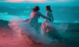 two young women in dresses dancing in the sand