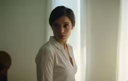 a woman standing in front of window and staring into camera