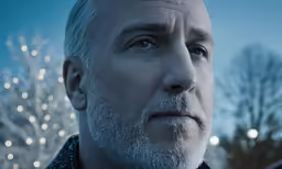 an older man stares straight ahead while standing outside