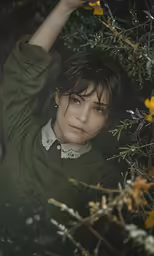 a young woman leaning against some bushes with her hand over her head