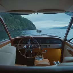 a view from inside a parked car of water with hills and forest on one side