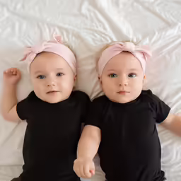 two babies on white sheets wearing pink bows