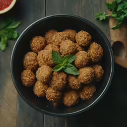 a bowl with meatballs and herbs in it