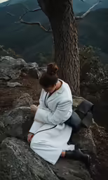a woman sitting on top of a rock near a tree
