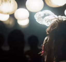 a girl in profile as a group of people watch with fireworks and lights behind her
