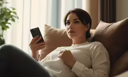 a woman is on the couch holding her cell phone