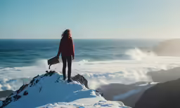 woman in red jacket on top of a snow covered mountain overlooking the ocean
