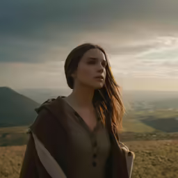 a woman wearing a brown coat and standing on a hillside