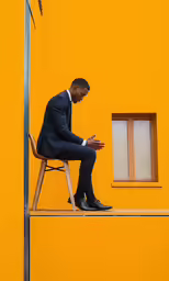 the man in a suit is sitting on a chair and using his phone