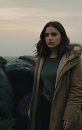 a woman in a trench coat standing on rocks