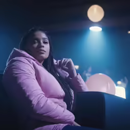 a black woman in a pink jacket sitting on the chair in a dark theater