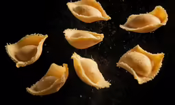 six dumplings are being made and served on a dark surface