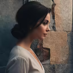 a woman leaning against a brick wall with her head tilted to her left