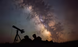 two people looking at stars from the ground and a telescope