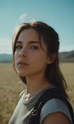 a woman in grey shirt and black backpack standing in a field