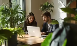 two people are sitting at a table with an apple laptop