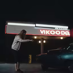 a woman standing in a parking lot next to a neon sign