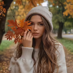 young woman in a white sweater holding leaves near trees