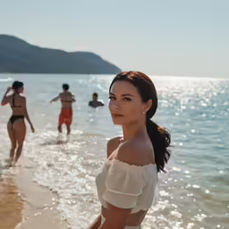 a woman walking on a beach with swimmers in the water
