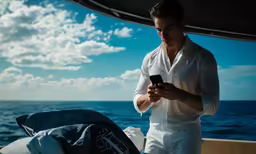 the man stands on the boat looking at his cell phone