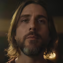a bearded man with long hair and a collared t - shirt