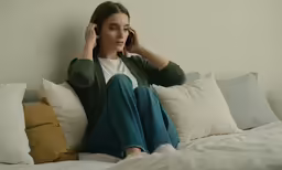 a young woman sitting on a bed using a cell phone