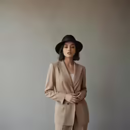 a woman in a suit and hat stands on the ground