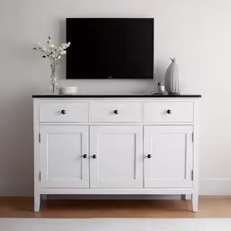 a tv is mounted above an empty white sideboard