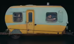 an old yellow and blue trailer with two people inside