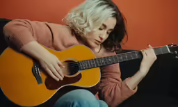 a woman sitting on a couch playing an acoustic guitar