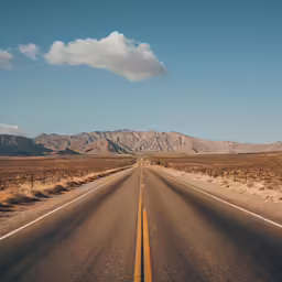 an empty, long road surrounded by mountains and trees