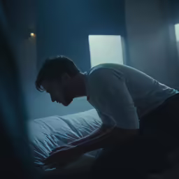 a man sits on a bed with his head down