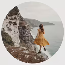 woman standing on the side of a cliff looking down at water