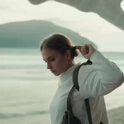a young woman looks down at her bag on the beach