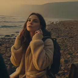 the woman sits on the beach talking on her cell phone