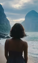 a woman stands on the beach in front of the mountains