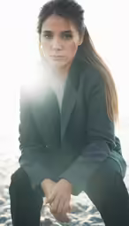 a woman wearing a suit and sitting on rocks with the sun shining through her hair