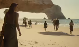 woman in green dress walking on beach with people in background